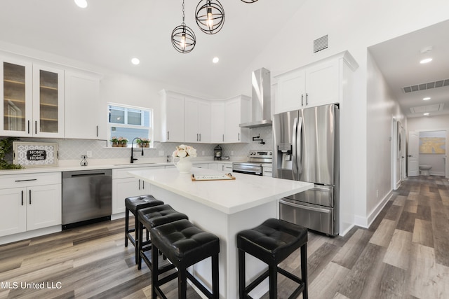 kitchen featuring wall chimney range hood, appliances with stainless steel finishes, sink, a kitchen breakfast bar, and dark hardwood / wood-style floors