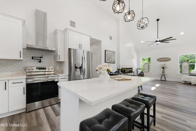 kitchen with wall chimney range hood, white cabinetry, high vaulted ceiling, dark hardwood / wood-style floors, and stainless steel appliances