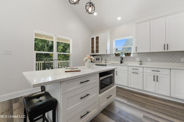 kitchen featuring stainless steel microwave, dark wood-type flooring, sink, white cabinets, and tasteful backsplash