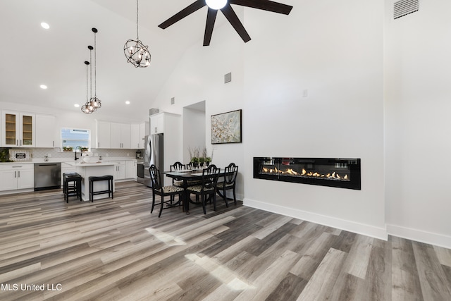 dining space with ceiling fan, high vaulted ceiling, sink, and light wood-type flooring