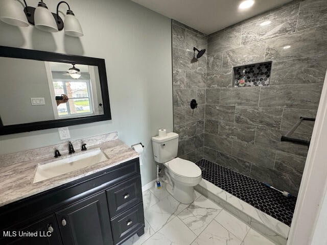 bathroom featuring toilet, ceiling fan, vanity, and tiled shower