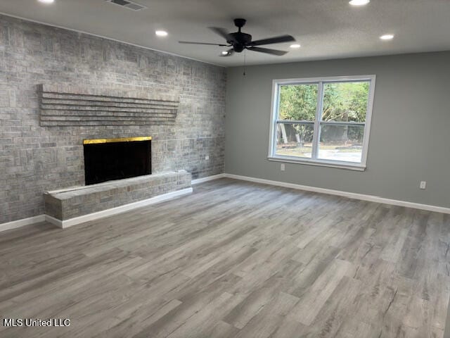 unfurnished living room with a brick fireplace, hardwood / wood-style flooring, and ceiling fan