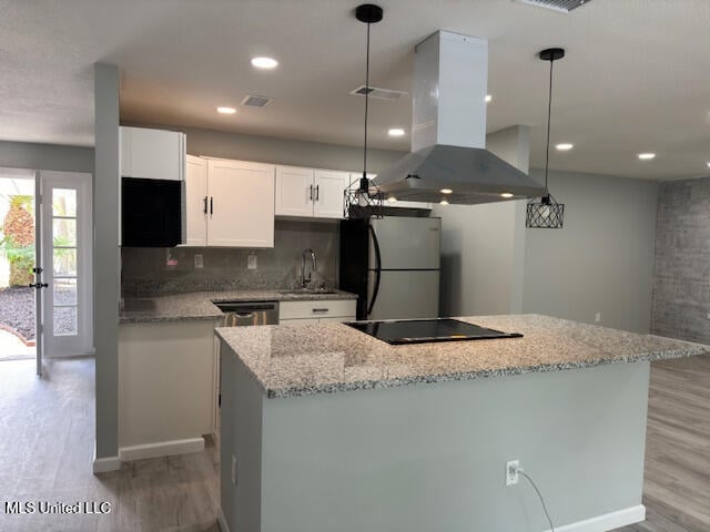 kitchen with black electric cooktop, island range hood, refrigerator, hanging light fixtures, and white cabinetry