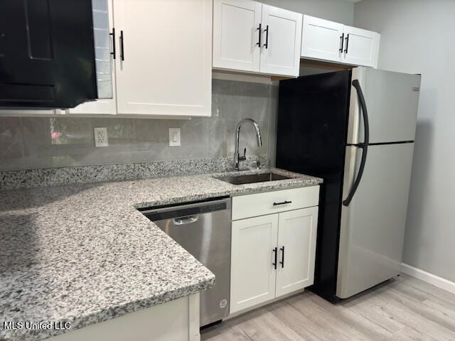 kitchen featuring light stone counters, stainless steel appliances, white cabinetry, sink, and light hardwood / wood-style floors