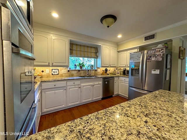 kitchen with appliances with stainless steel finishes, white cabinetry, light stone counters, ornamental molding, and dark hardwood / wood-style floors