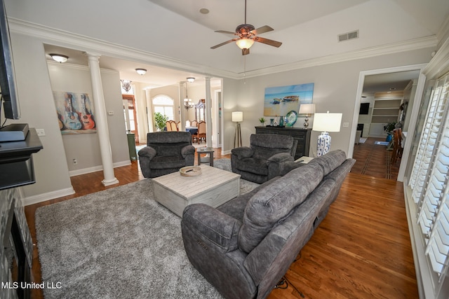 living room with dark wood-type flooring, ceiling fan with notable chandelier, ornamental molding, and decorative columns