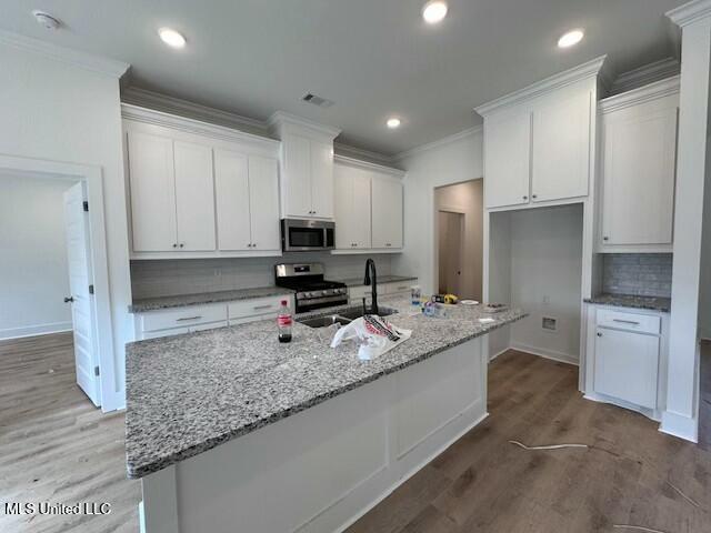 kitchen with white cabinetry, a kitchen island with sink, stainless steel appliances, sink, and crown molding