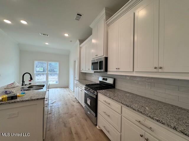 kitchen with stainless steel appliances, light stone counters, decorative backsplash, sink, and white cabinetry