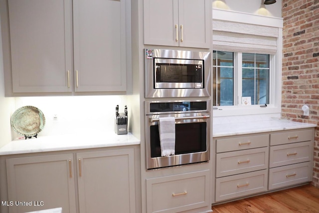 kitchen featuring stainless steel microwave, light wood-style flooring, and brick wall