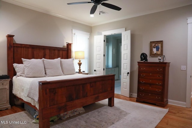 bedroom with visible vents, crown molding, baseboards, ensuite bathroom, and wood finished floors