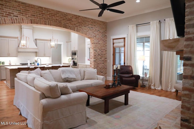 living area with brick wall, a ceiling fan, arched walkways, and light wood finished floors