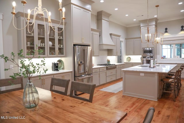 kitchen with light wood-type flooring, a notable chandelier, ornamental molding, appliances with stainless steel finishes, and hanging light fixtures