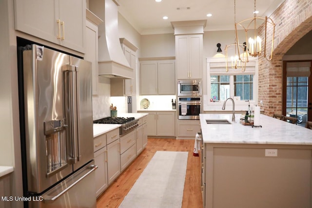 kitchen with premium range hood, an island with sink, a sink, stainless steel appliances, and a chandelier