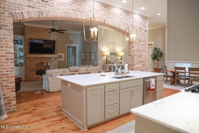 kitchen featuring a sink, open floor plan, light wood finished floors, a brick fireplace, and dishwasher