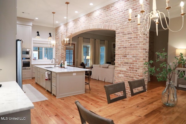 dining room featuring brick wall, crown molding, light wood-style floors, an inviting chandelier, and arched walkways