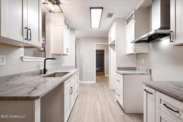 119 Vance Cv, Byhalia, MS 38611 - kitchen with wall chimney exhaust hood, a sink, light wood finished floors, light stone counters, and baseboards