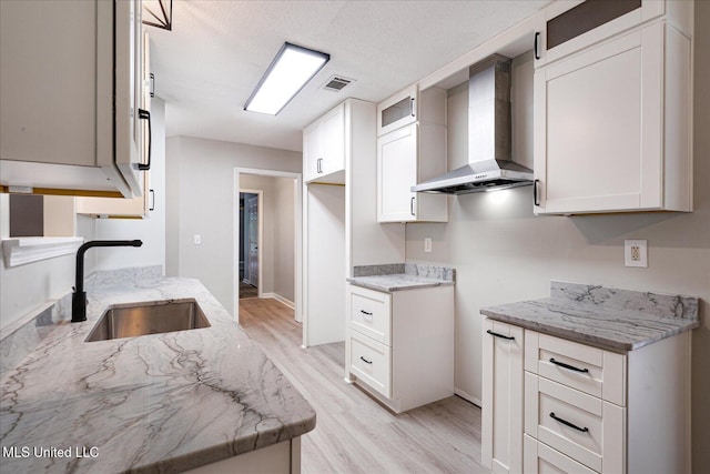 119 Vance Cv, Byhalia, MS 38611 - kitchen with a sink, wall chimney exhaust hood, light stone counters, light wood-style flooring, and glass insert cabinets