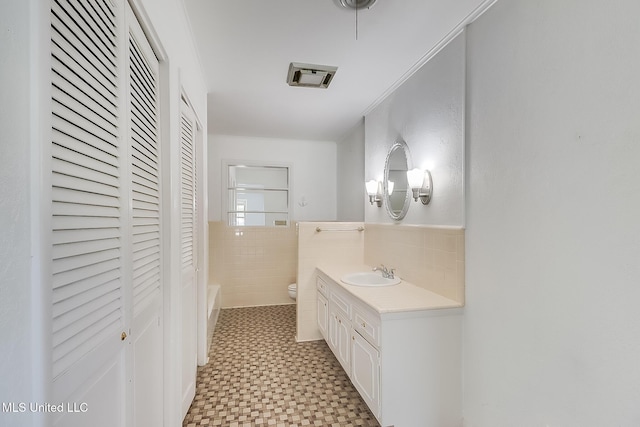 bathroom with vanity, toilet, tile walls, and ornamental molding