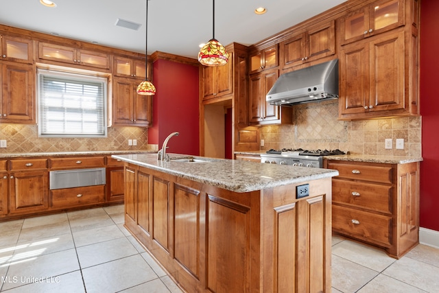 kitchen with decorative backsplash, a center island with sink, sink, pendant lighting, and light stone counters