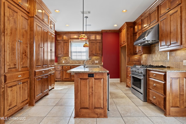 kitchen with hanging light fixtures, an island with sink, light stone countertops, stainless steel range, and sink