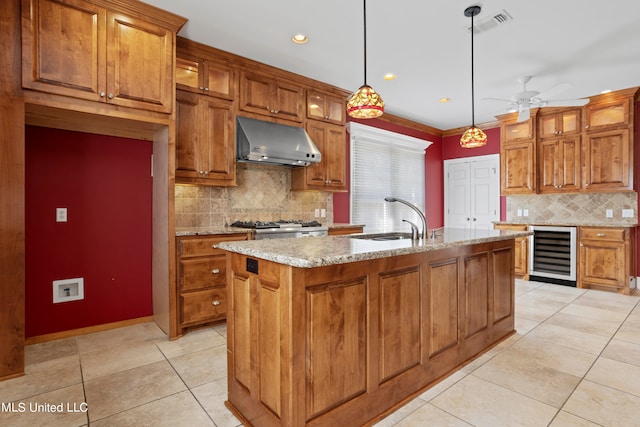 kitchen with exhaust hood, an island with sink, sink, pendant lighting, and beverage cooler