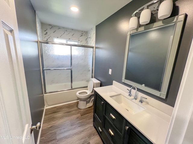 full bathroom featuring toilet, vanity, wood-type flooring, and combined bath / shower with glass door