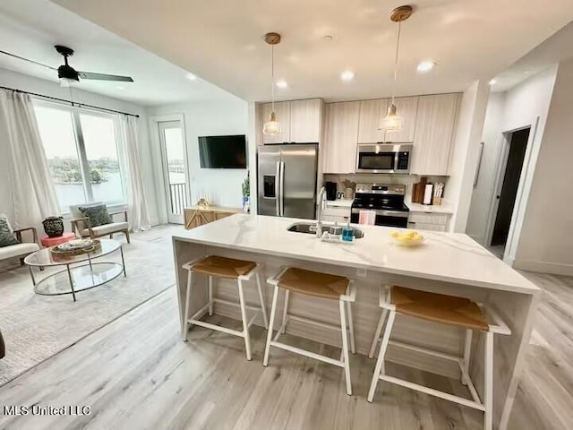 kitchen with sink, hanging light fixtures, a center island with sink, stainless steel appliances, and a kitchen bar