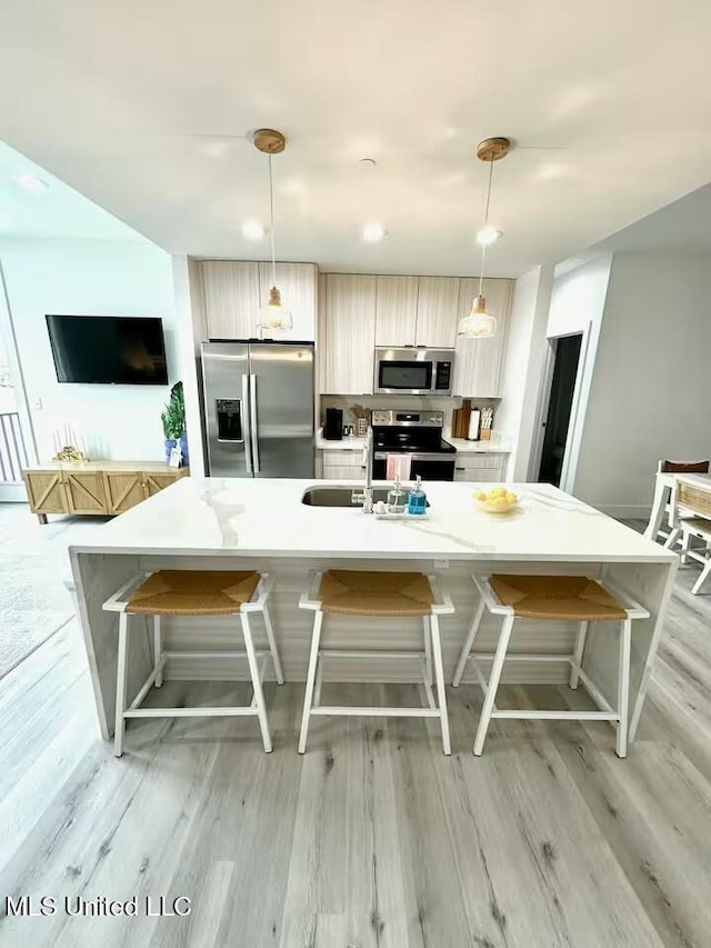 kitchen with pendant lighting, stainless steel appliances, sink, and a center island with sink