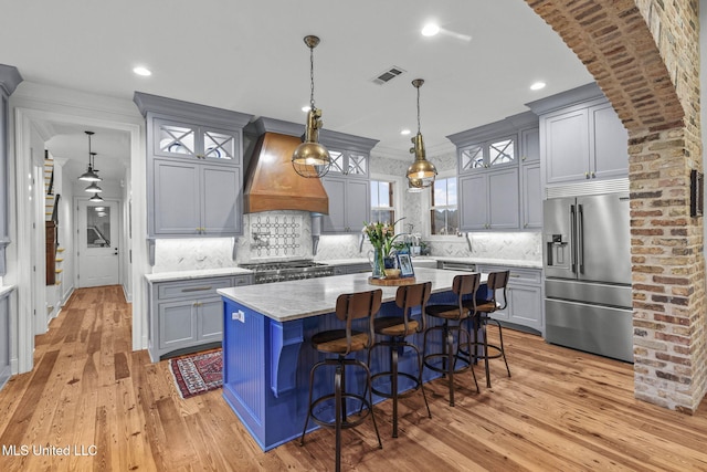 kitchen with pendant lighting, stainless steel appliances, a center island, custom range hood, and a kitchen bar