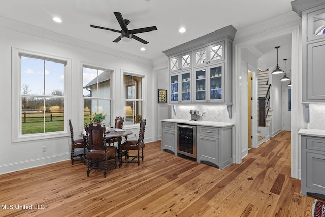 kitchen featuring wine cooler, crown molding, light wood-type flooring, and gray cabinetry