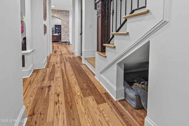 corridor with brick wall and light hardwood / wood-style flooring