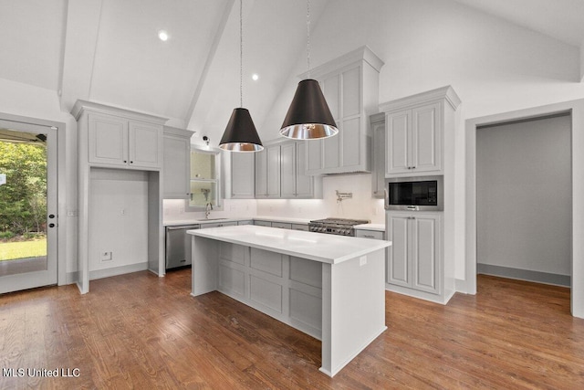 kitchen featuring stainless steel appliances, sink, wood-type flooring, high vaulted ceiling, and a center island