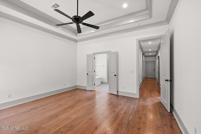 unfurnished bedroom with a tray ceiling, ensuite bath, ceiling fan, and hardwood / wood-style flooring