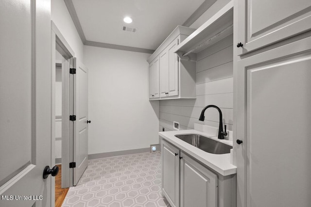 laundry area with electric dryer hookup, crown molding, sink, and cabinets