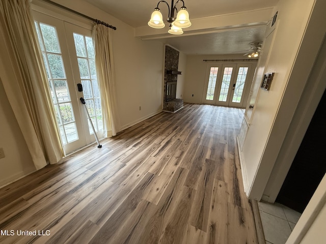 unfurnished dining area featuring baseboards, wood finished floors, french doors, a fireplace, and a notable chandelier