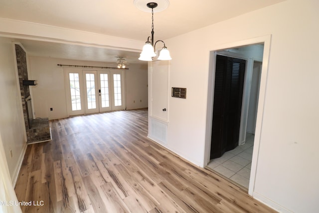 empty room with baseboards, light wood-style flooring, ceiling fan, french doors, and a fireplace