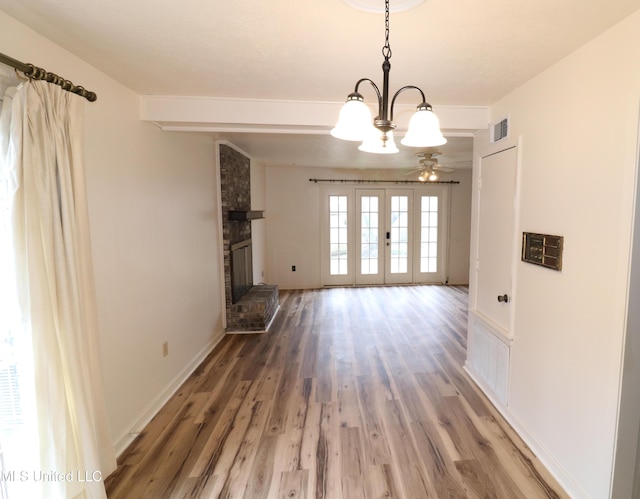 unfurnished dining area with visible vents, wood finished floors, french doors, a brick fireplace, and beam ceiling