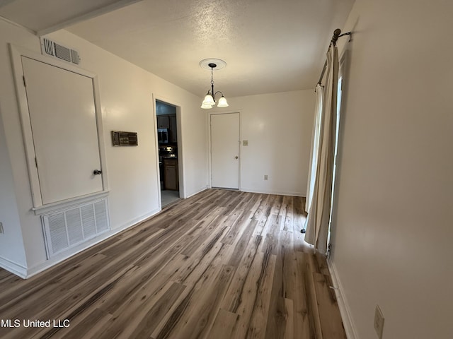 unfurnished dining area featuring dark wood-style flooring, visible vents, a notable chandelier, and baseboards