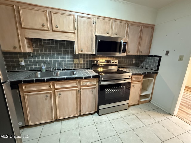 kitchen with stainless steel appliances, tile counters, decorative backsplash, light tile patterned flooring, and a sink