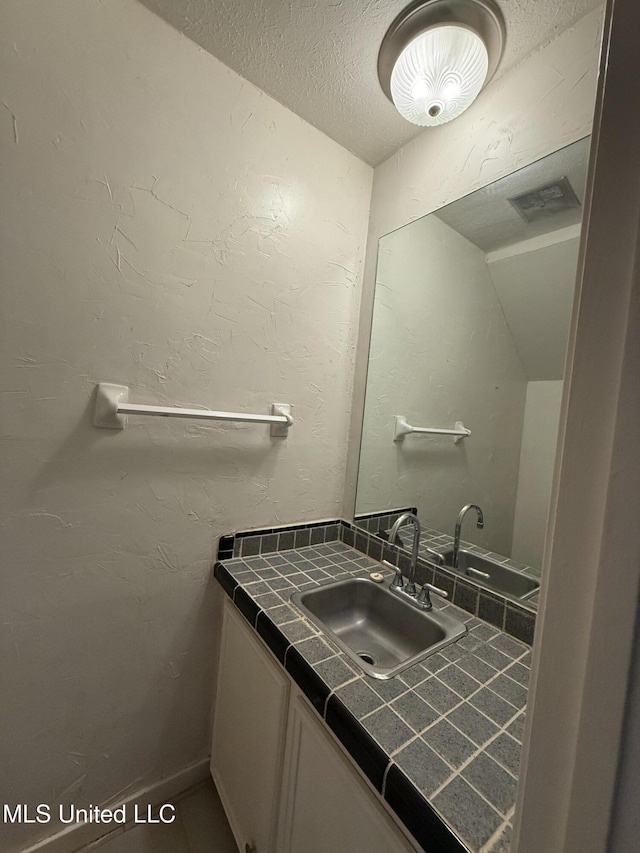 bathroom featuring vanity, visible vents, a textured ceiling, and a textured wall