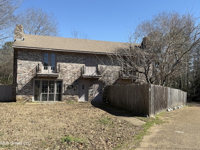 rear view of property with a chimney, fence, and brick siding