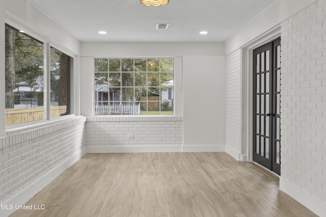 interior space with brick wall, light hardwood / wood-style flooring, and a wealth of natural light