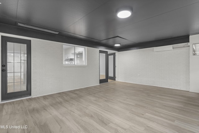 basement featuring brick wall, light wood-type flooring, and a wall unit AC