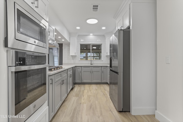 kitchen featuring stainless steel appliances, light wood-type flooring, backsplash, and gray cabinetry