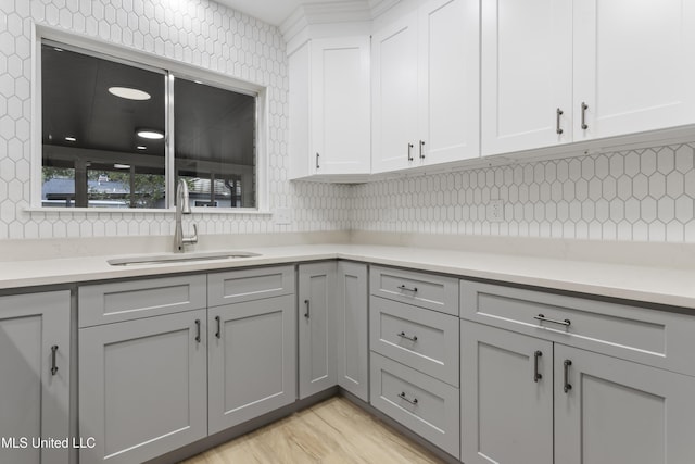 kitchen with decorative backsplash, white cabinetry, gray cabinetry, and sink