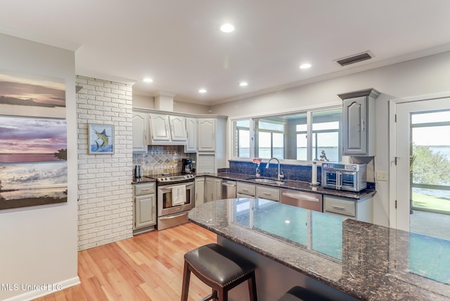 435 Christi Ln, Biloxi, MS 39531 - kitchen featuring stainless steel appliances, tasteful backsplash, dark stone counters, light wood-style floors, and a breakfast bar