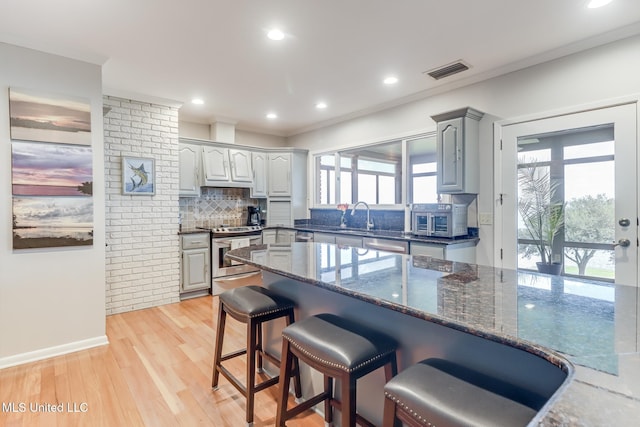 435 Christi Ln, Biloxi, MS 39531 - kitchen featuring stainless steel electric range, a breakfast bar area, decorative backsplash, dark stone countertops, and light wood-style flooring