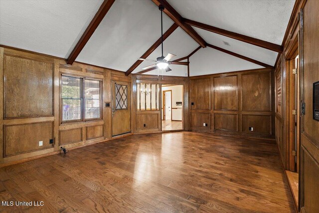 spare room featuring lofted ceiling with beams, a decorative wall, a ceiling fan, wooden walls, and dark wood-type flooring
