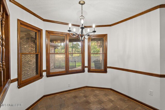 spare room with stone finish floor, ornamental molding, baseboards, a notable chandelier, and a textured ceiling