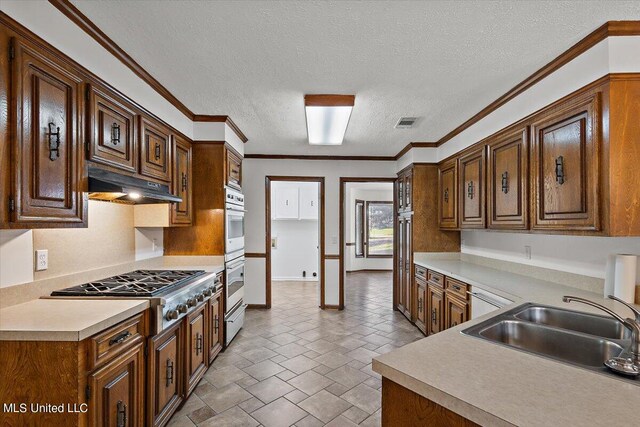 kitchen with double oven, stainless steel gas cooktop, ornamental molding, sink, and a textured ceiling